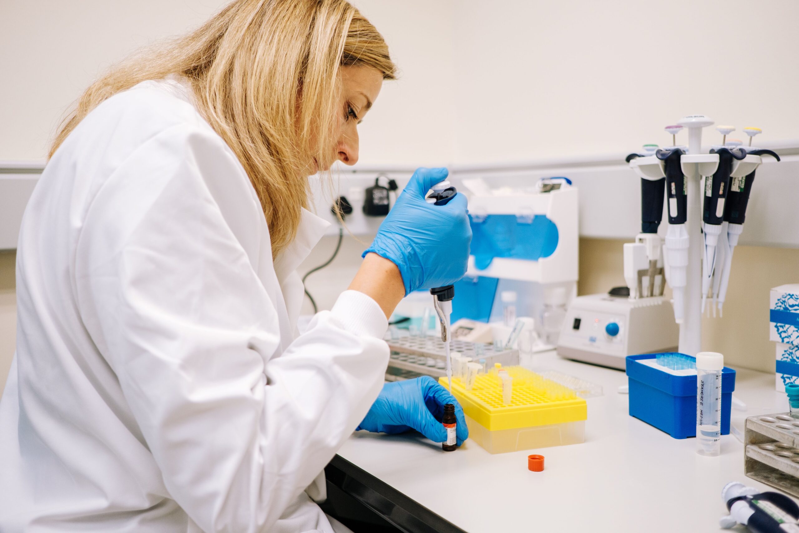 Dr Chloe George in white coat sitting at bench with scientific equipment